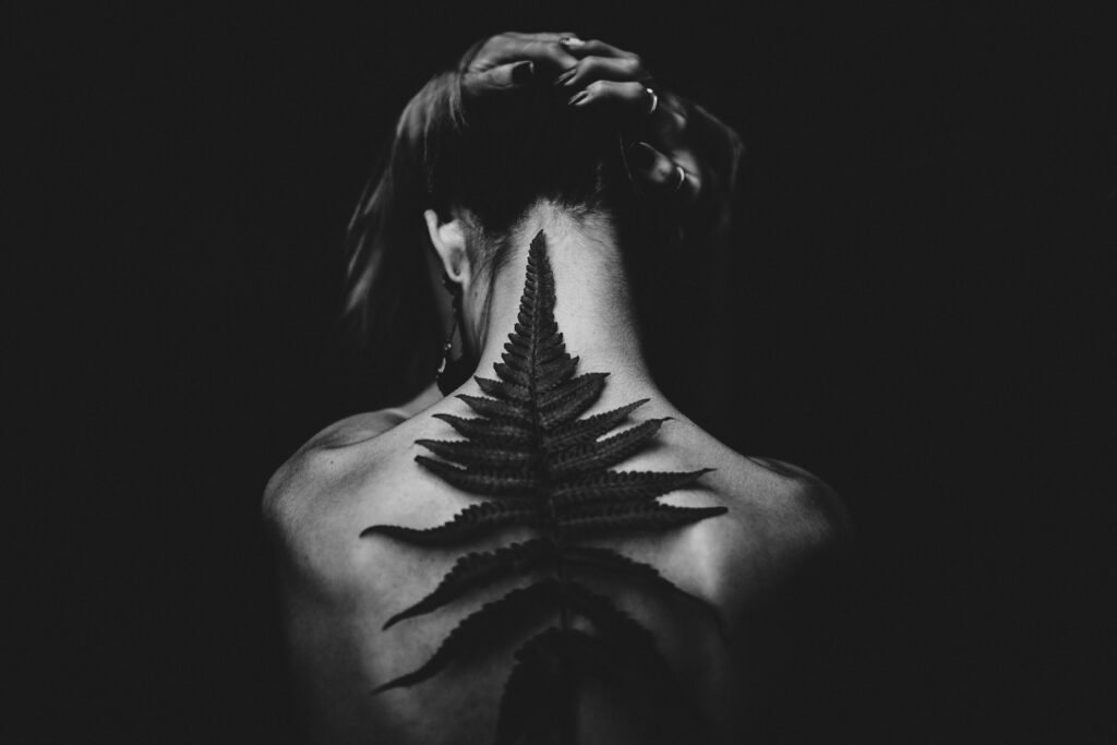 Black and white photo of a tattooed woman from the back, featuring a fern design. Captivating and artistic pose.